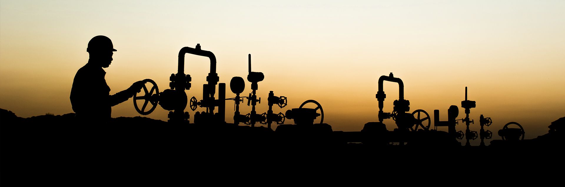 Silhouette of a field worker operating wellhead valves at sunset